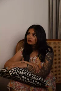 Modelling image of Reshma Das. A lady with free hair, sitting on a chair, pillow on her lap, looking at someone confused