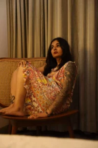Modelling image of Reshma Das. A lady in casual attire, sitting on a couch with legs on the couch, with a thoughtful expression on face